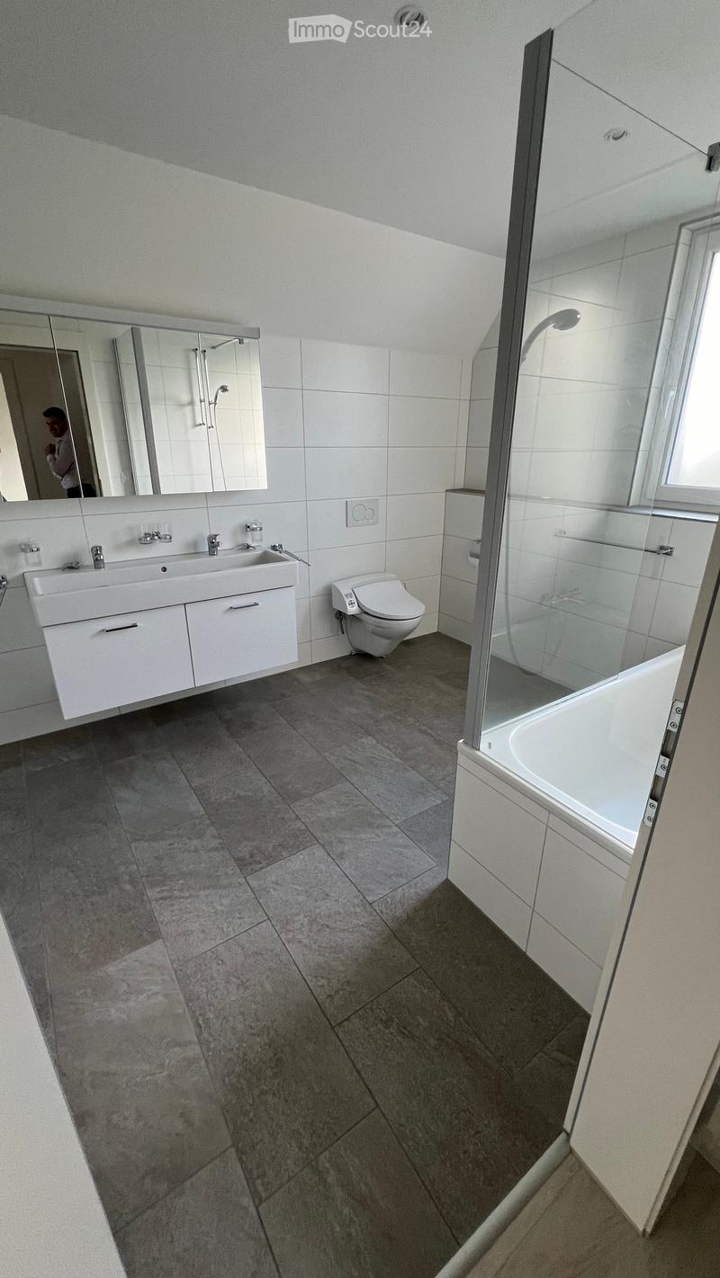 Modern bathroom with white tiles, a double sink, a toilet, a bathtub, and a glass-enclosed shower area.