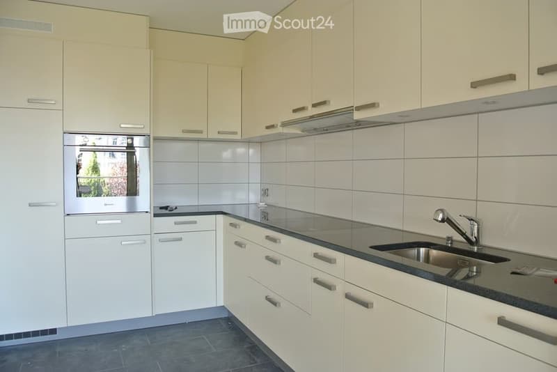 Modern kitchen with white cabinets, stainless steel sink, and built-in oven. Features a sleek design with a black countertop and grey tiles on the floor.