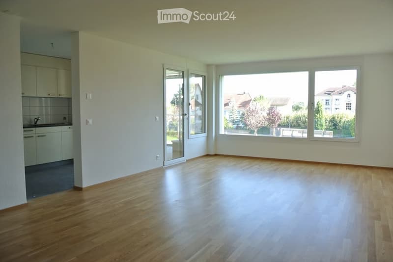 Empty room with wooden flooring, white walls, large windows, and a sliding glass door leading to a balcony.