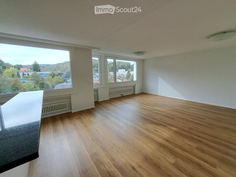 Empty room with wooden flooring, large windows offering a scenic view, and white walls.