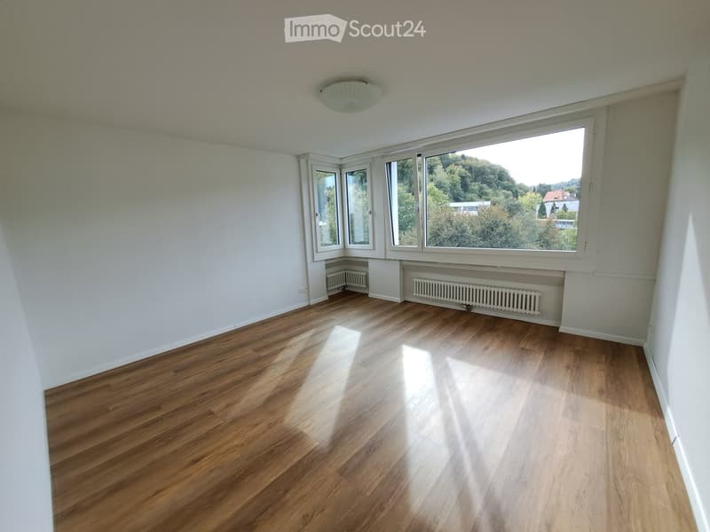 Empty room with wooden flooring, white walls, large windows, and radiators. No furniture or equipment present.