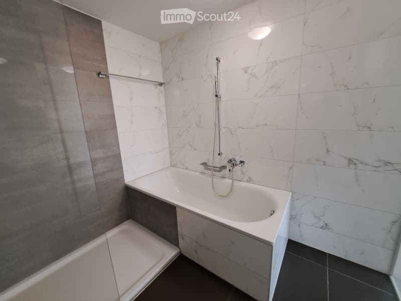Modern bathroom with a white bathtub, marble tiles, a glass shower enclosure, and a towel rack.