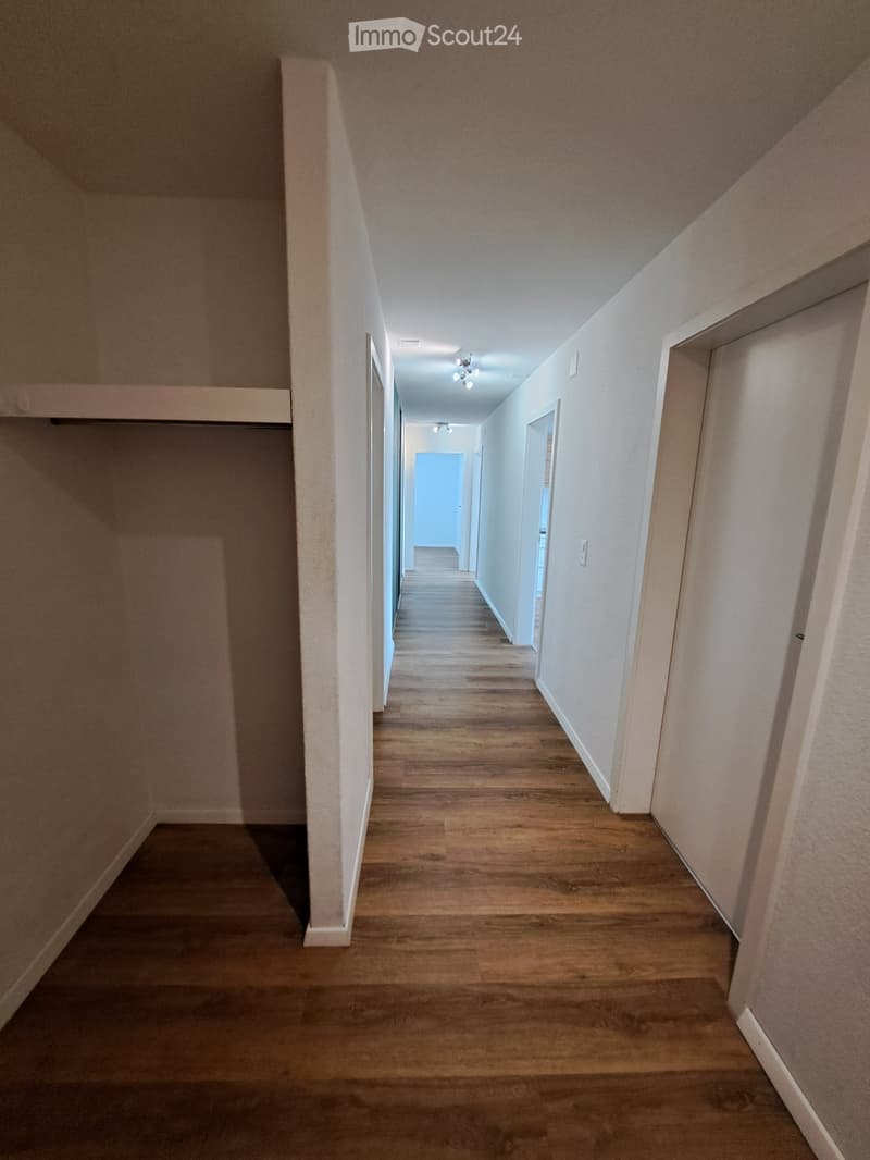 Empty hallway with wooden flooring, white walls, and several doors leading to other rooms.