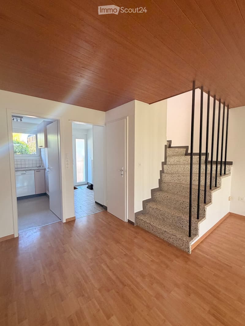 Spacious hallway with wooden flooring, a staircase with a modern metal railing, and open doors leading to other rooms.