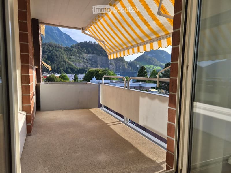 Balcony with carpeted floor, white railings, and a yellow and white striped awning, overlooking a scenic mountain landscape.