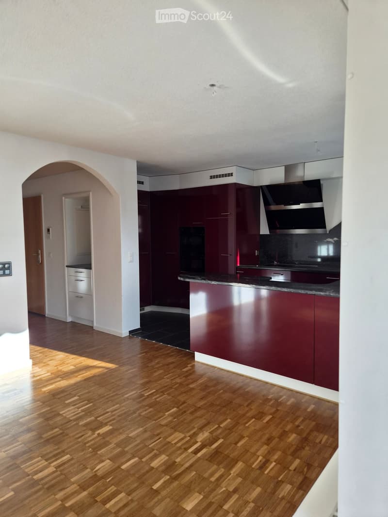 Modern kitchen with dark red cabinets, a black countertop, and a stainless steel oven. The floor is wooden, and the space is well-lit with natural light.