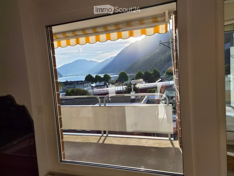 Balcony with a view of mountains and a lake, featuring a striped awning and a glass railing.