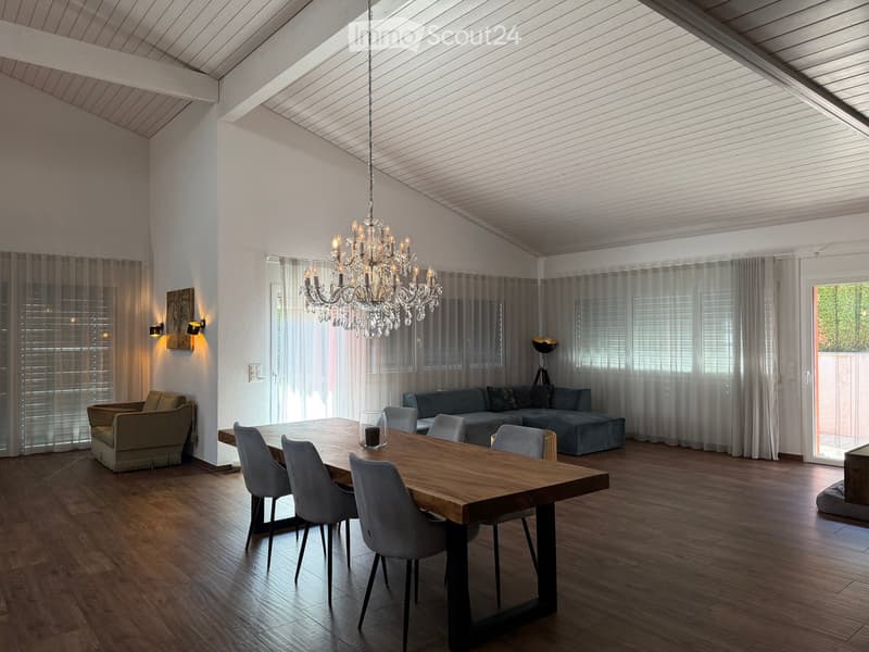 Open-concept living and dining area with wooden flooring, a chandelier, a dining table with chairs, a sofa, and wall and floor lamps.