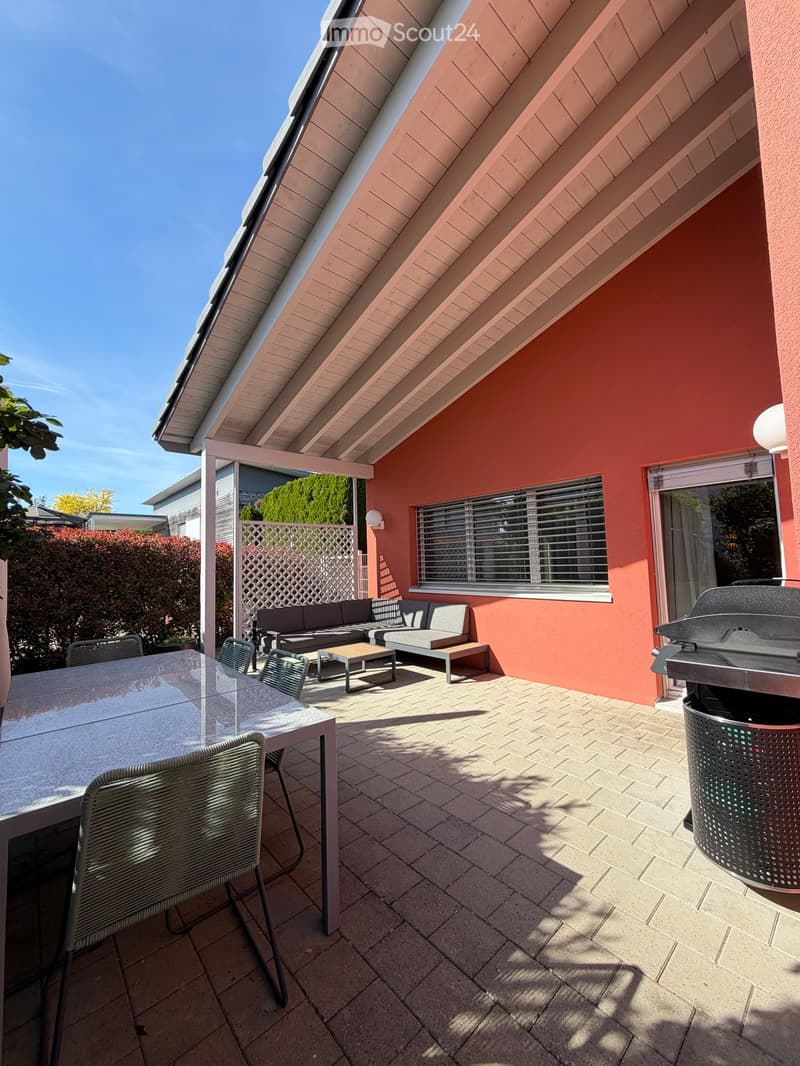 Outdoor patio with a covered roof, tiled floor, and seating area including a sofa, coffee table, and dining table with chairs.