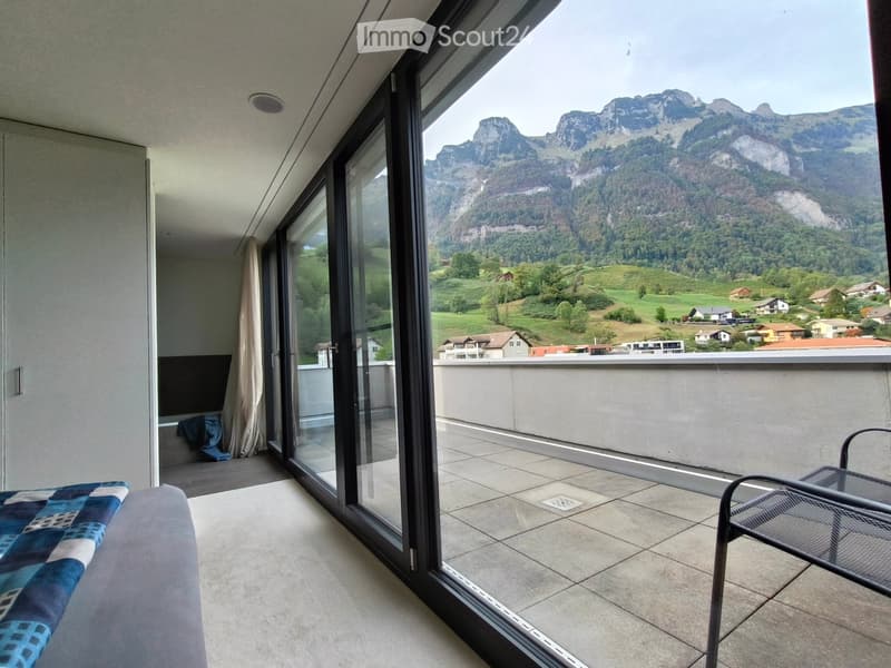 Balcony with a scenic mountain view, tiled floor, and a single metal chair.