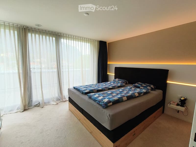 Modern bedroom with a large bed, blue patterned bedding, built-in storage, and a nightstand with a lamp.