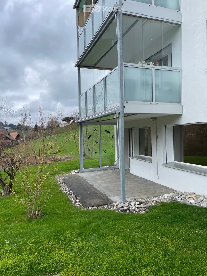 Modern two-story house with large glass balcony and white exterior, surrounded by a well-maintained lawn and pathway.