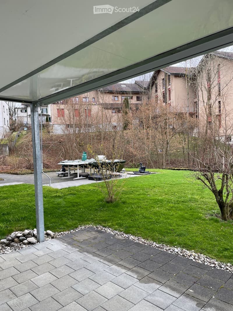 Garden area with a paved patio, grassy lawn, and a covered outdoor seating area with a table and benches.