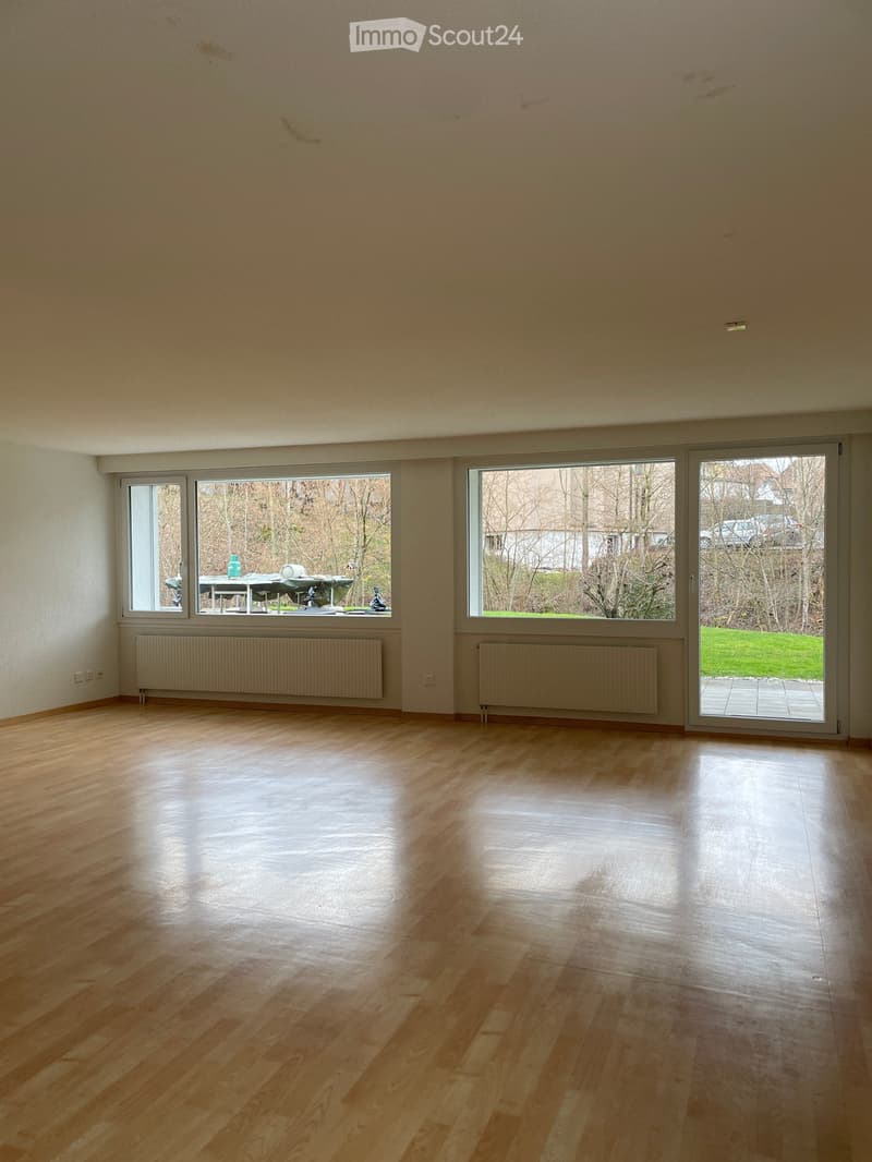 Empty room with wooden flooring, large windows, radiators, and a sliding glass door leading to an outdoor area.