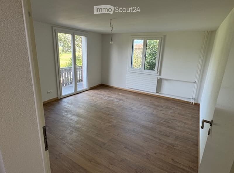 Empty room with wooden flooring, large window, and sliding glass door leading to a balcony.