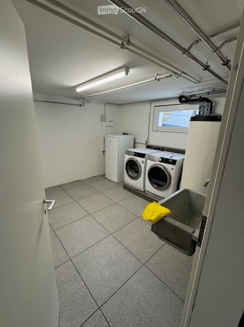 Small utility room with tiled floor, white walls, fluorescent lighting, washing machine, refrigerator, sink, and a yellow towel.
