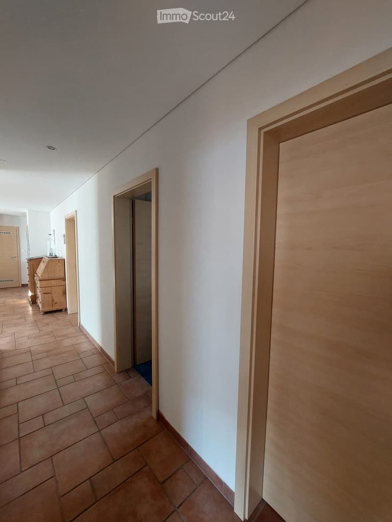 Empty hallway with tiled floor, white walls, and several wooden doors leading to other rooms.