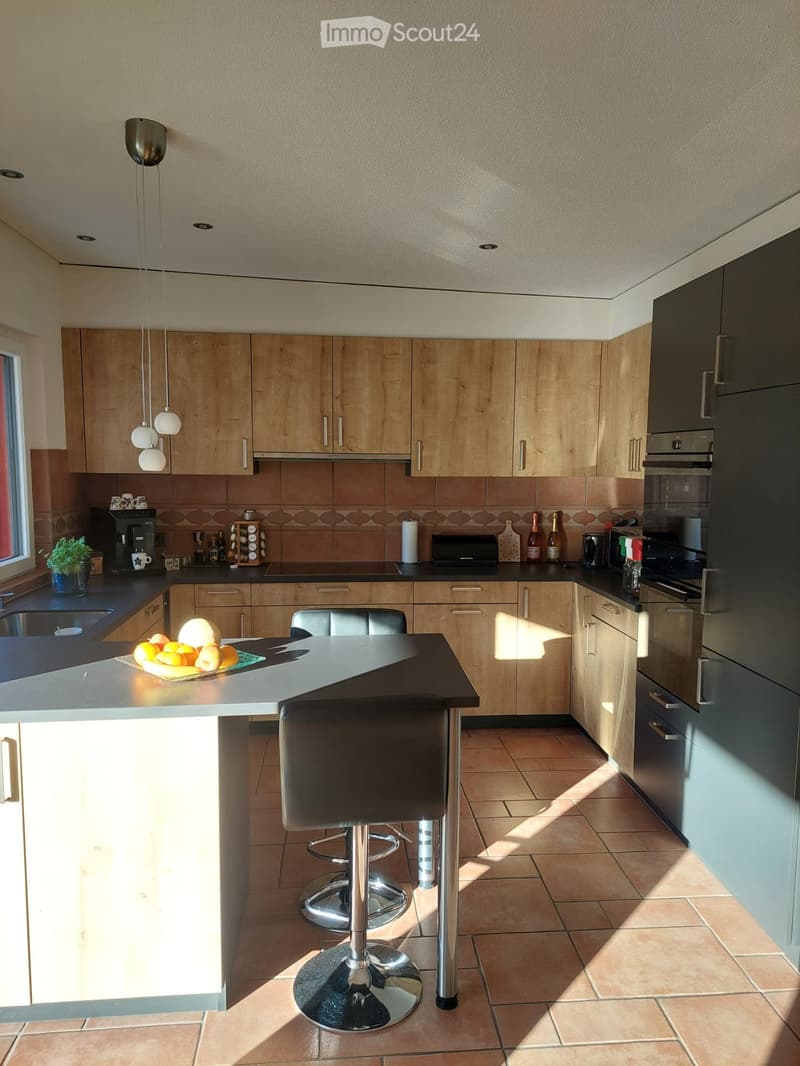 Modern kitchen with wooden cabinets, stainless steel appliances, island with bar stools, and various kitchen items on the counter.