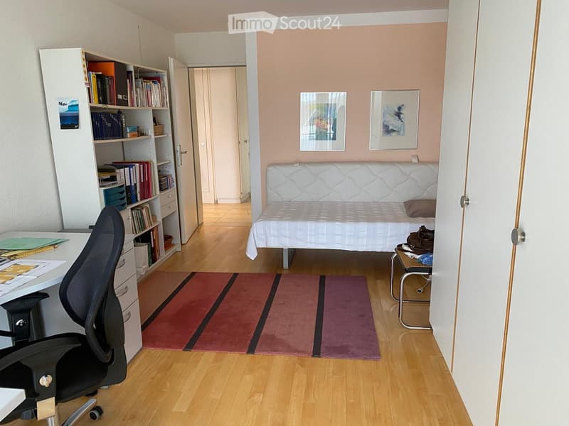 A furnished room with a sofa, chair, desk, bookshelf, and picture frames on the wall.