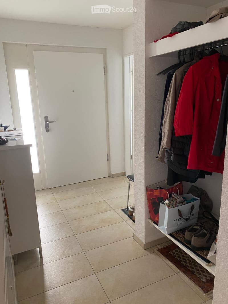 Hallway with tiled floor, white walls, a closet with hanging clothes, and a small table with items on it.