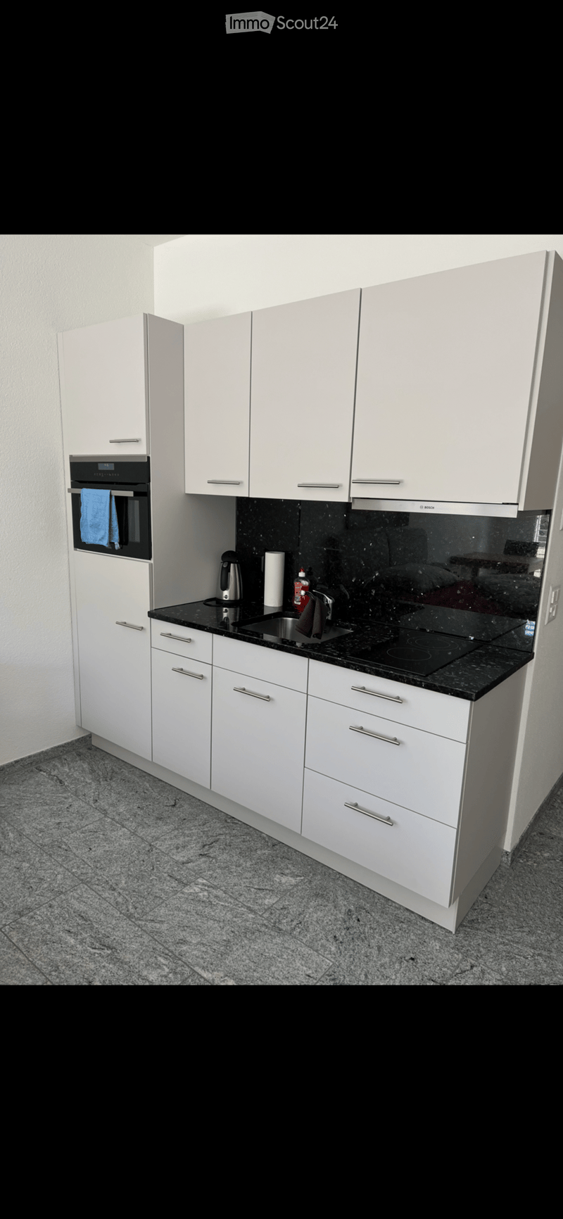 Modern kitchen with white cabinets, black granite countertops, and stainless steel appliances including an oven, sink, and electric kettle.