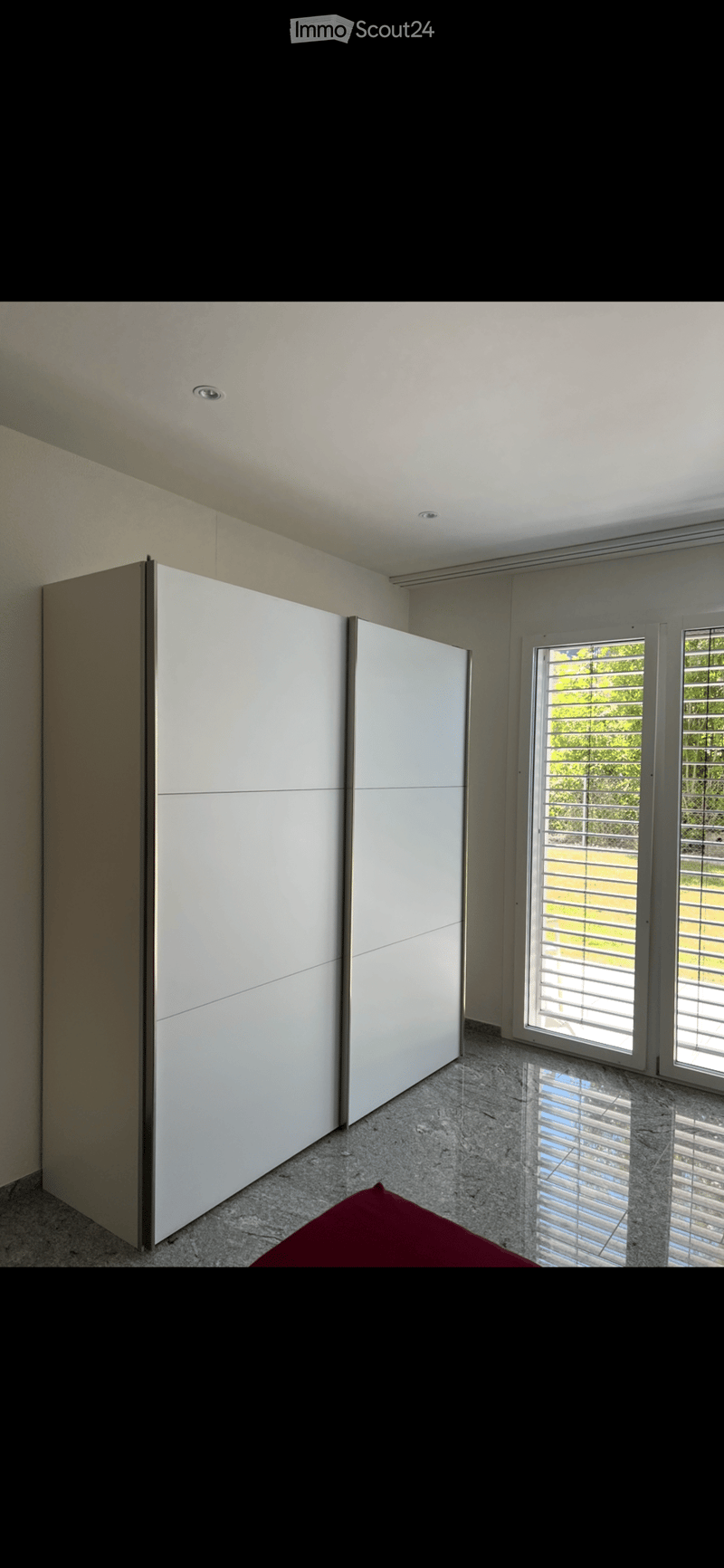 Modern, minimalist room with a large white wardrobe, polished marble floor, and large windows with blinds.
