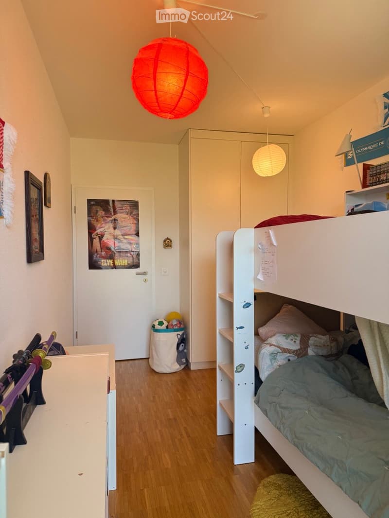 A cozy bedroom with a bunk bed, a wardrobe, a framed picture on the wall, and a colorful lamp hanging from the ceiling.