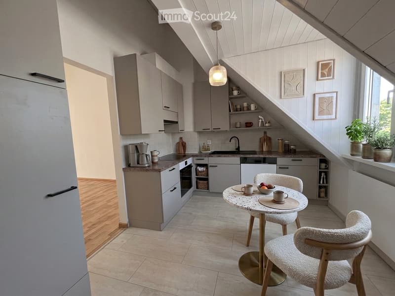 Modern kitchen with white cabinets, stainless steel appliances, a small dining area with a round table and chairs, and decorative items on the windowsill.