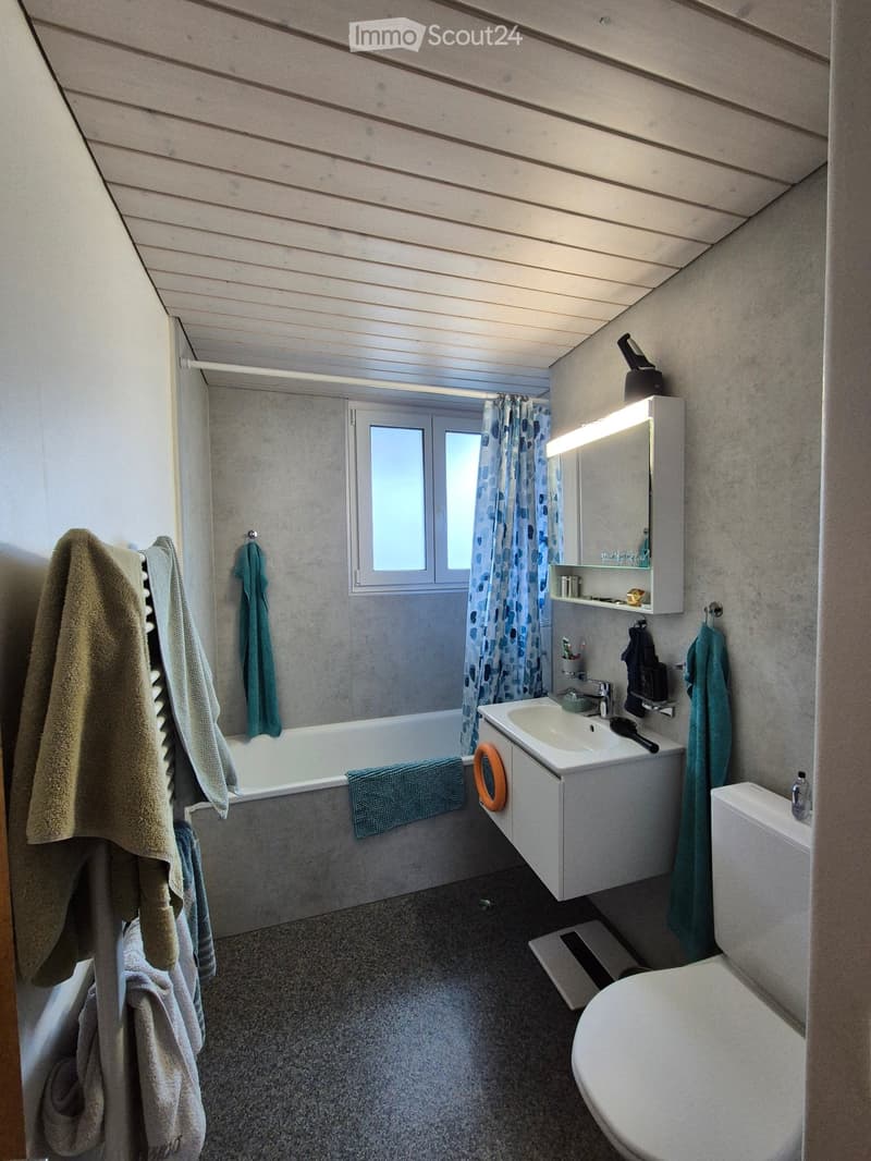 Bathroom with a bathtub, sink, toilet, mirror, and towels. Features a window with a curtain and a built-in storage cabinet.