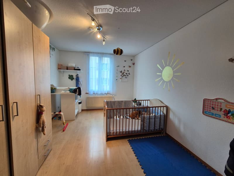 Brightly decorated children's bedroom with a crib, wardrobe, shelves, and various toys and decorations including a sun wall decoration and butterfly wall decorations.