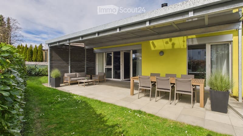 Modern outdoor patio with a covered seating area, dining table, and lawn.