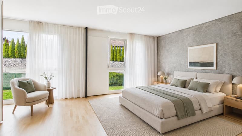 Modern bedroom with a large bed, nightstands, a chair, and a small table near the window. The room features light wooden flooring, large windows with sheer curtains, and a textured grey accent wall.