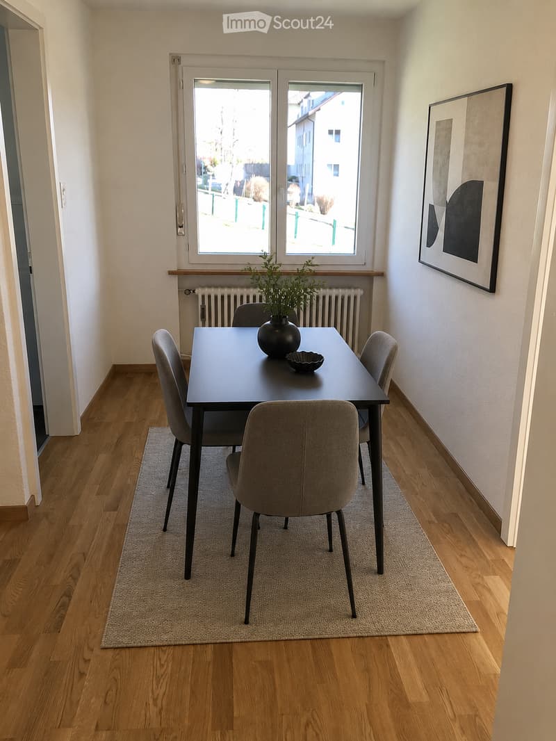 Dining area with a dark wooden table, four grey chairs, a vase with greenery, and a bowl on the table. Light wooden flooring and a small rug under the table.