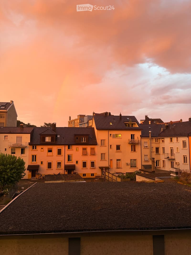 Residential buildings with multiple stories, dark roofs, and balconies, viewed from a rooftop perspective during sunset.