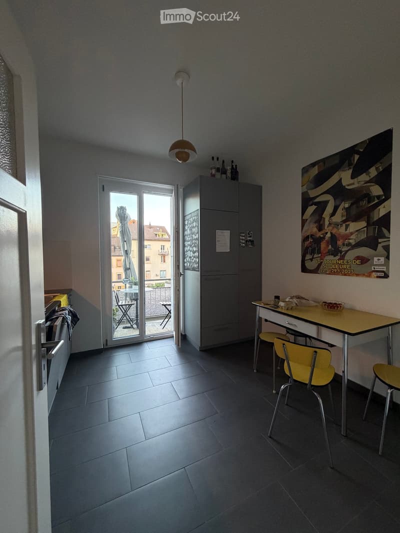 A modern kitchen with a dining area, featuring a table with chairs, a cabinet, a fridge, and a balcony access.