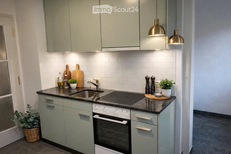 Modern kitchen with light grey cabinets, dark countertops, and stainless steel appliances including an oven, sink, and faucet. Wooden cutting boards, potted plants, and decorative items are on the countertops.