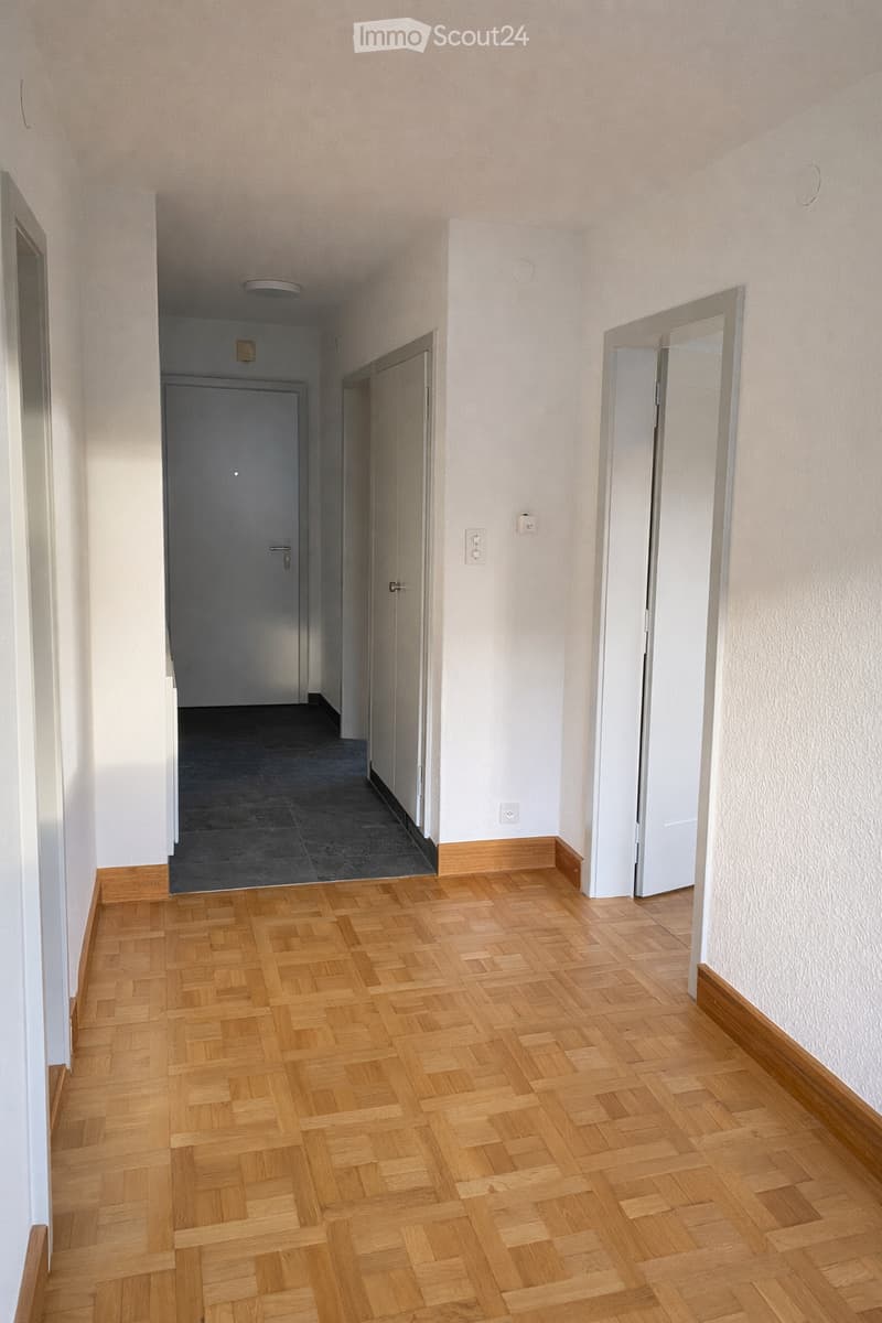 Empty hallway with wooden herringbone flooring, white walls, and several doors leading to other rooms.