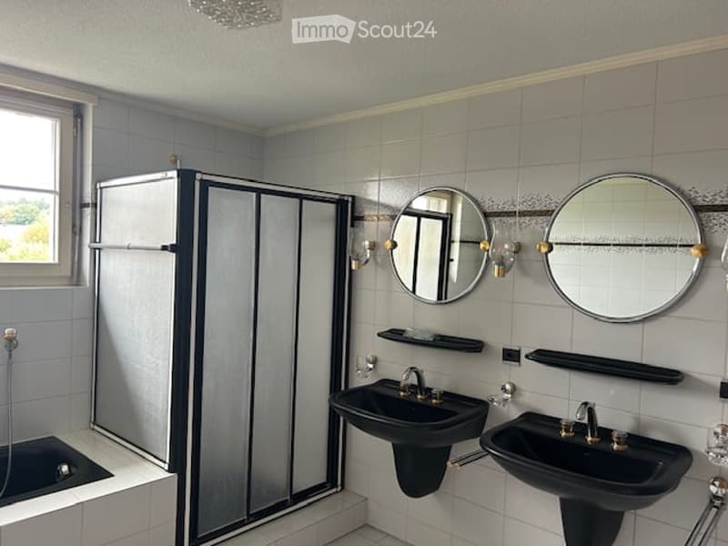 A bathroom with a bathtub, two black sinks, a walk-in shower, two round mirrors, and chrome-finished fixtures