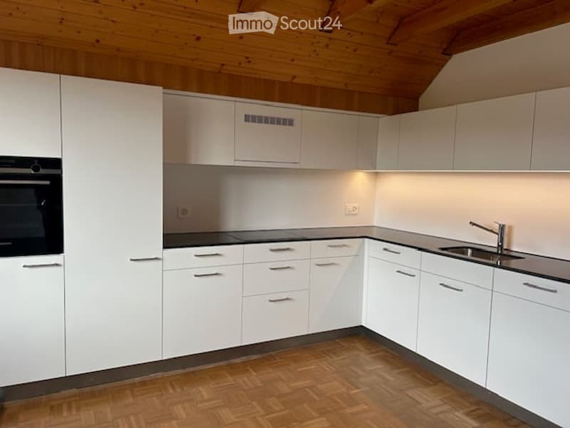 Modern kitchen with white cabinets, wooden flooring, and built-in appliances including an oven and sink.