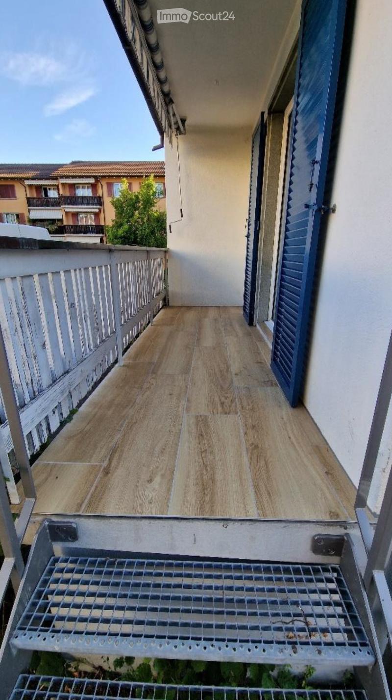 Balcony with wooden flooring, white railing, and blue shutters on adjacent building.