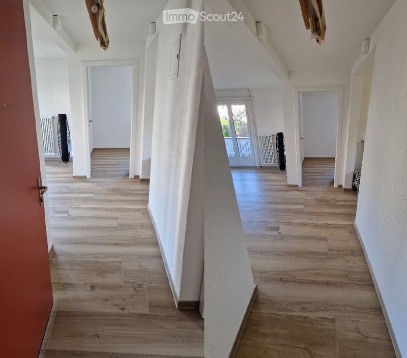 Empty hallway with wooden flooring, white walls, and several doors leading to other rooms.