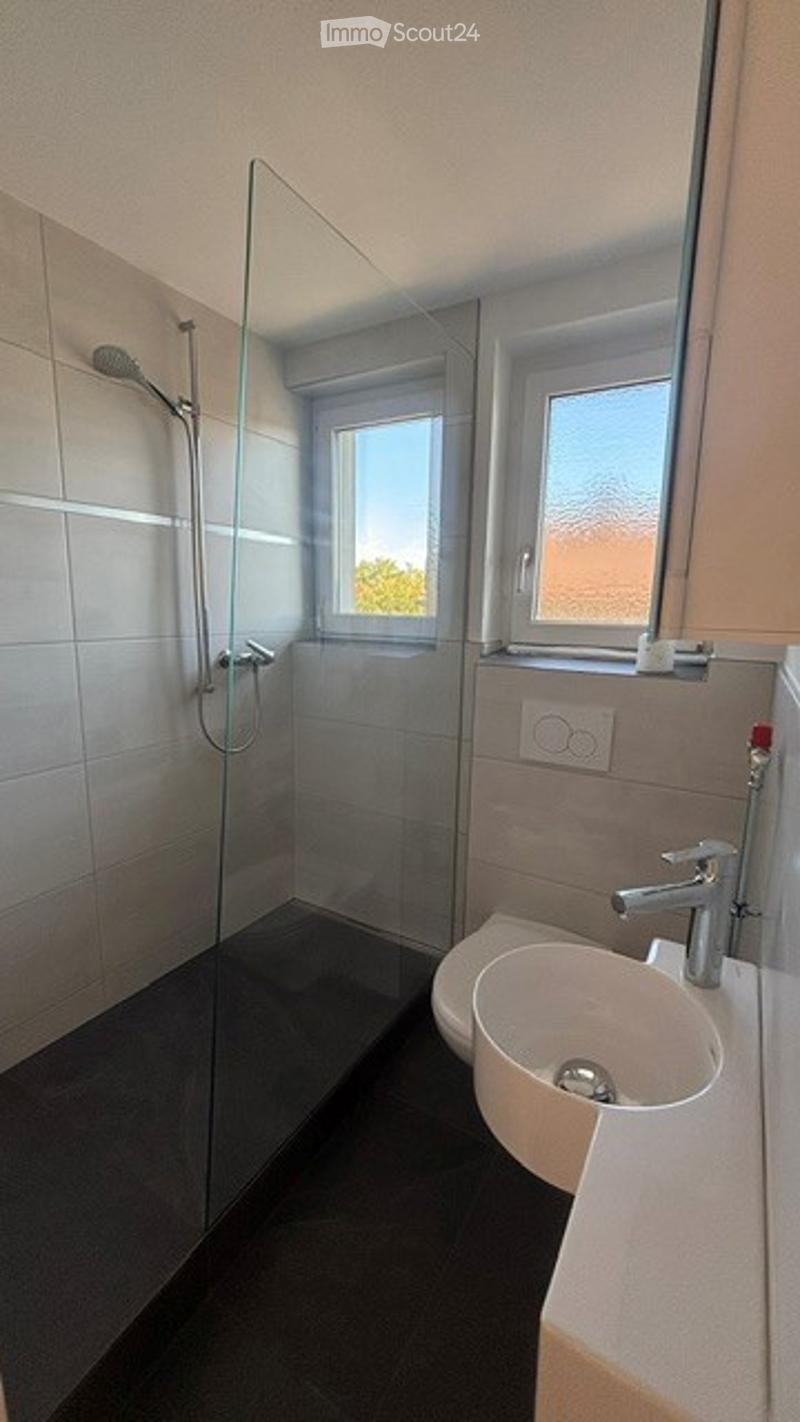 Modern bathroom with a glass-enclosed shower, a white sink with a chrome faucet, and a window providing natural light.