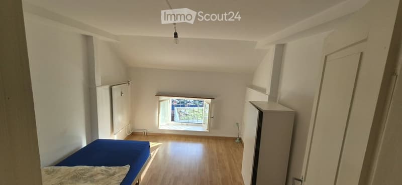 Bright bedroom with wooden flooring, a single bed with blue bedding, a window opening to a balcony, and built-in storage units.