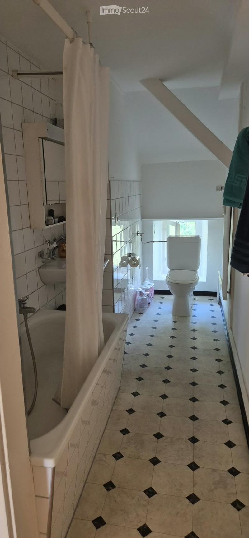 Bathroom with a bathtub, toilet, sink, and shower curtain. The floor has a patterned tile design, and there is a small window providing natural light.