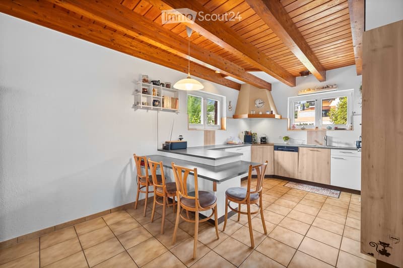 Bright kitchen with wooden beams, island seating, modern appliances, and ample natural light from windows.