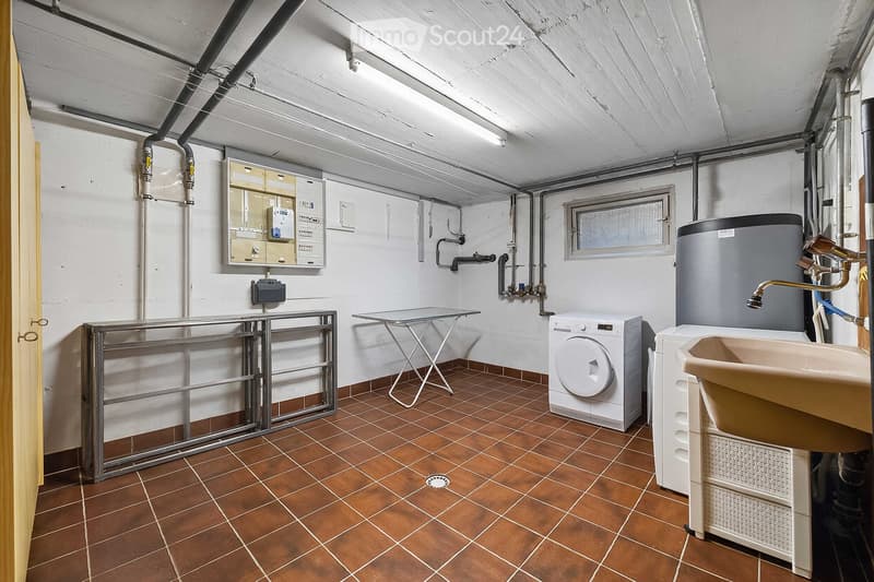 Utility room with tiled floor, washing machine, sink, and various pipes and fixtures.