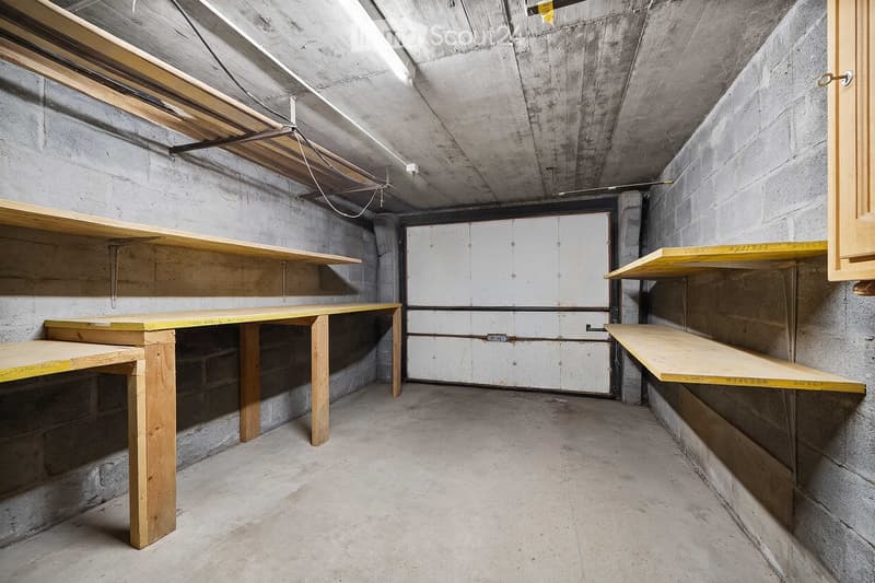 Empty basement or storage room with concrete walls and floor, wooden shelves, and exposed ceiling beams.