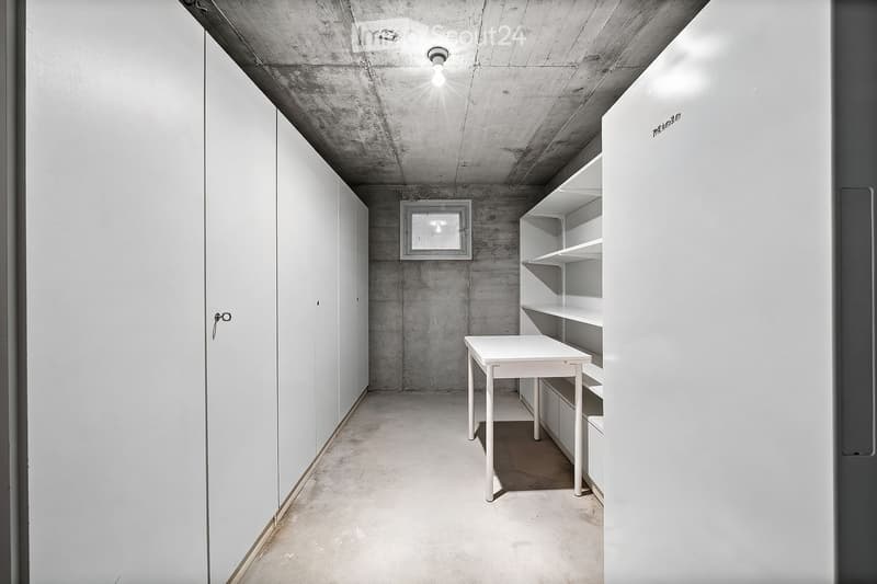 Minimalist room with concrete walls and ceiling, white table, built-in shelves, and a small window.