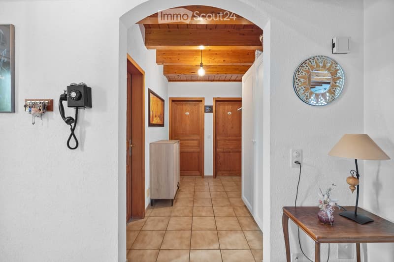 A well-lit hallway with wooden doors, a small wooden cabinet, a wall-mounted telephone, a decorative mirror, and a table lamp on a small table.