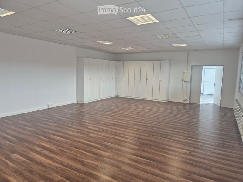 Empty room with wooden flooring, white walls, and a row of white lockers along one wall. The ceiling features recessed lighting panels.